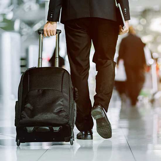 Businessman checking e mail on mobile phone while walking with suitcase inside airport